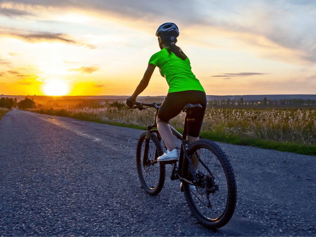 female cyclist riding on a road along a field at sunset