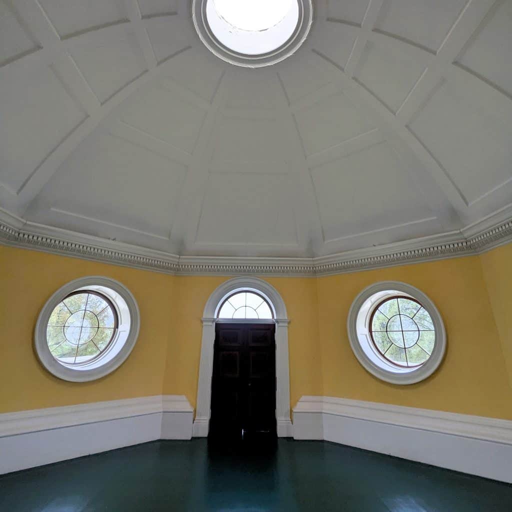 A circular domed room with round windows and a white ceiling, yellow walls and green floor.