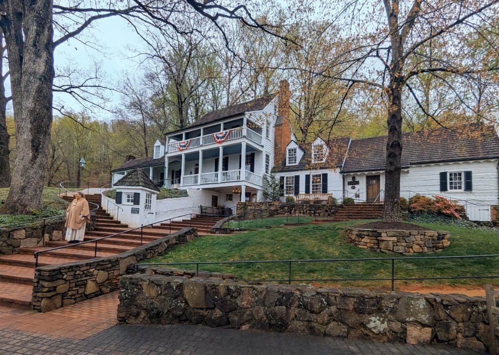 A historic inn surrounded by trees and has a stone walkway and stairs.