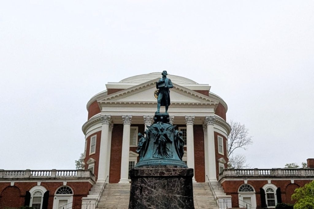 A statue of a man standing in front of a domed building.